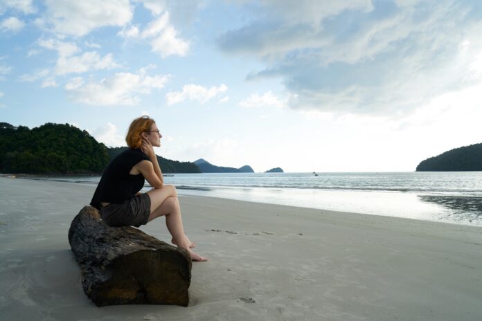 A woman gazes thoughtfully at the horizon by the shore, symbolizing the introspection and hope often associated with adrenal fatigue recovery.
