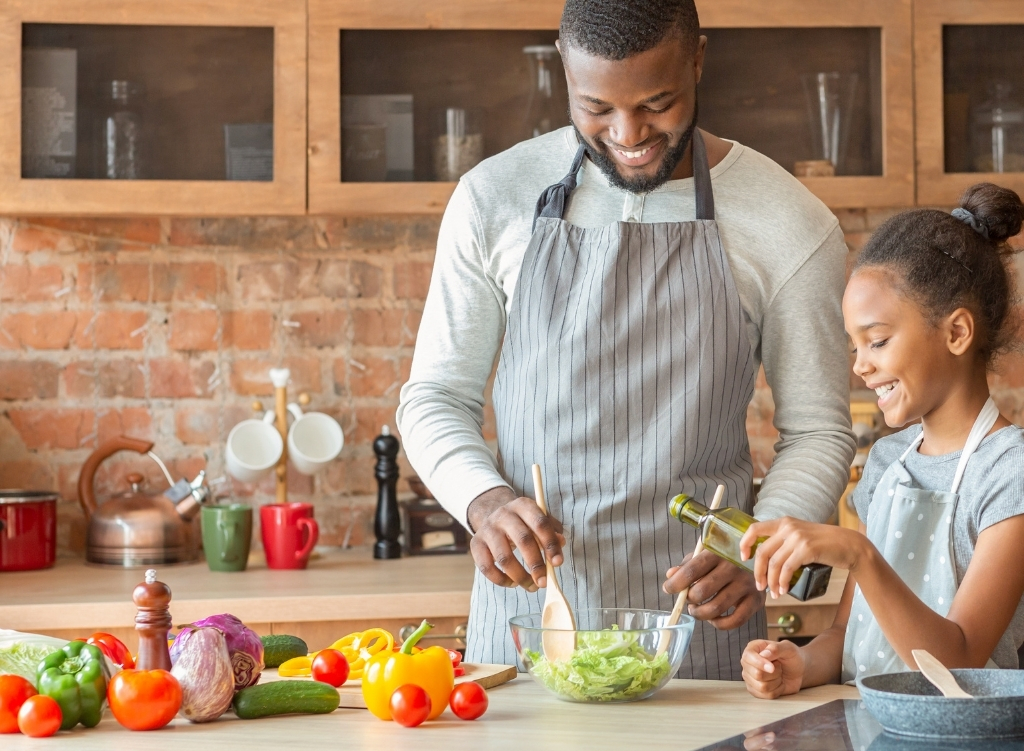 A father and daughter smiling while preparing a colorful salad in a kitchen, symbolizing the importance of family and healthy eating in functional medicine.