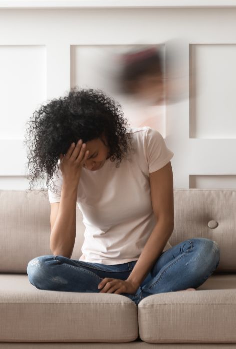 A person, hunched over on a couch, holds their head in their hands, their silhouette blurred to convey the dizziness and disorientation of a headache.