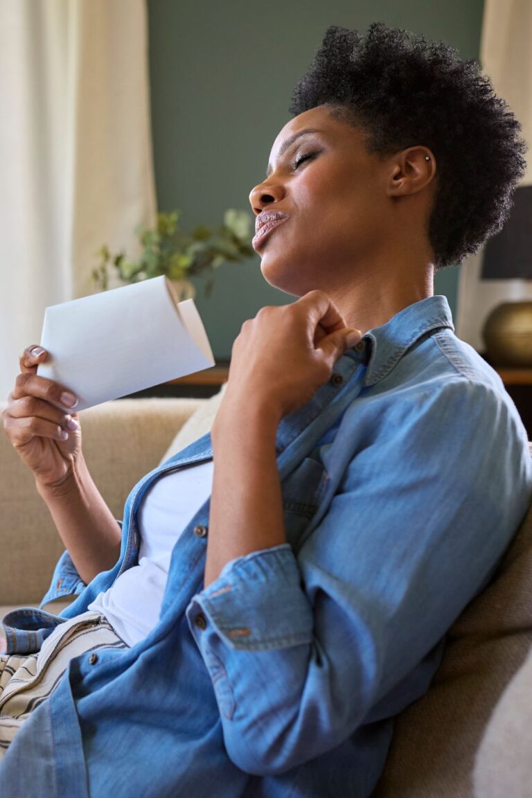 A woman cools herself with a fan, experiencing a hot flash during perimenopause.