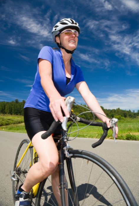 A smiling woman in her 40s cycling outdoors, enjoying the sunshine and fresh air,