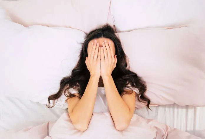 Frustrated woman covering eyes in bed, unable to sleep due to insomnia, seeking help from Five Journeys for cortisol-related sleep issues.