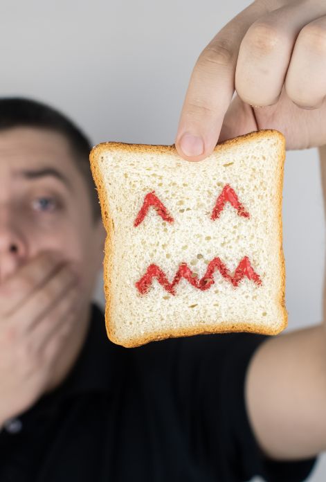 A man holding a piece of bread with a frowning face drawn on it, representing the negative emotions associated with gluten intolerance.