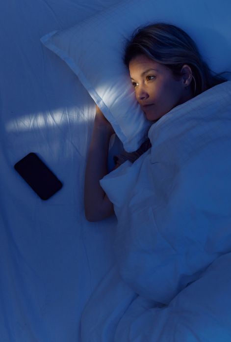 A woman lies awake in bed, bathed in the morning light, her expression reflecting the mental and emotional toll of insomnia.