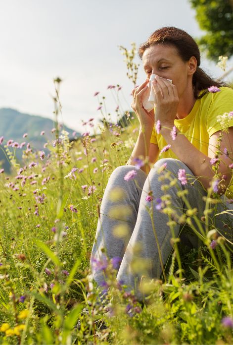 A woman sitting amidst a field of colorful flowers, surrounded by pollen, a bittersweet scene for those with seasonal allergies.