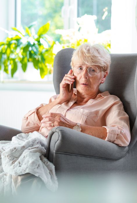 An elderly woman sits on a sofa, phone to her ear, her eyes conveying worry and concern, hinting at the anxieties that can accompany aging.