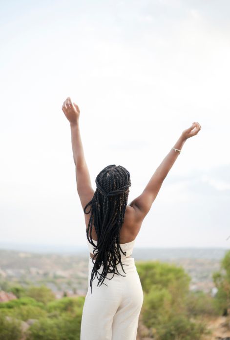 A Black woman in athletic wear, beaming with joy, raises her arms in celebration of her health and well-being, symbolizing the positive impact of overcoming menstrual irregularities.