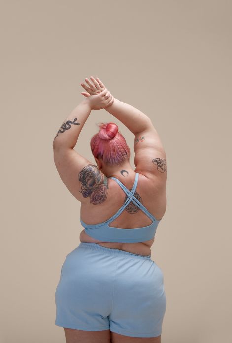 A curvy woman in workout clothes stretches her arms and legs, demonstrating the importance of flexibility and movement in achieving overall health and well-being.