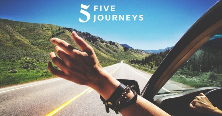 A person's arm reaches out the car window on a scenic road trip, with a sense of freedom and motion as they travel through a lush, green mountain landscape under a clear blue sky.